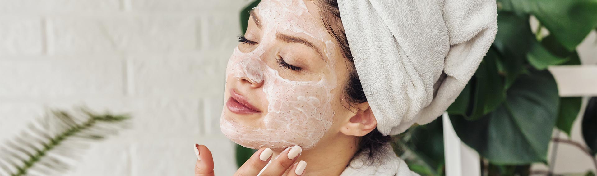 A woman cleansing her face with a towel covering her hair.