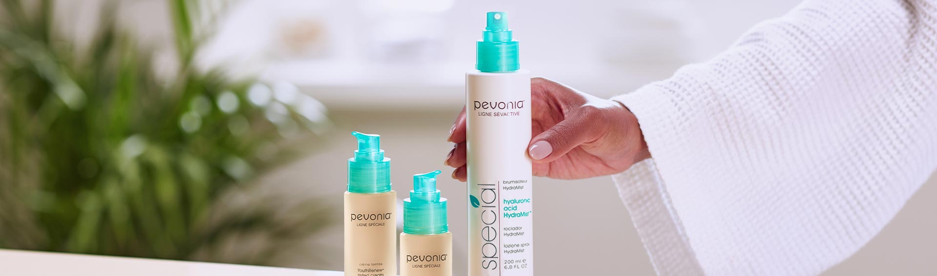 Woman reaching for Pevonia's Hyaluronic Acid HydraMist, which is standing near two YouthRenew Tinted Creams.