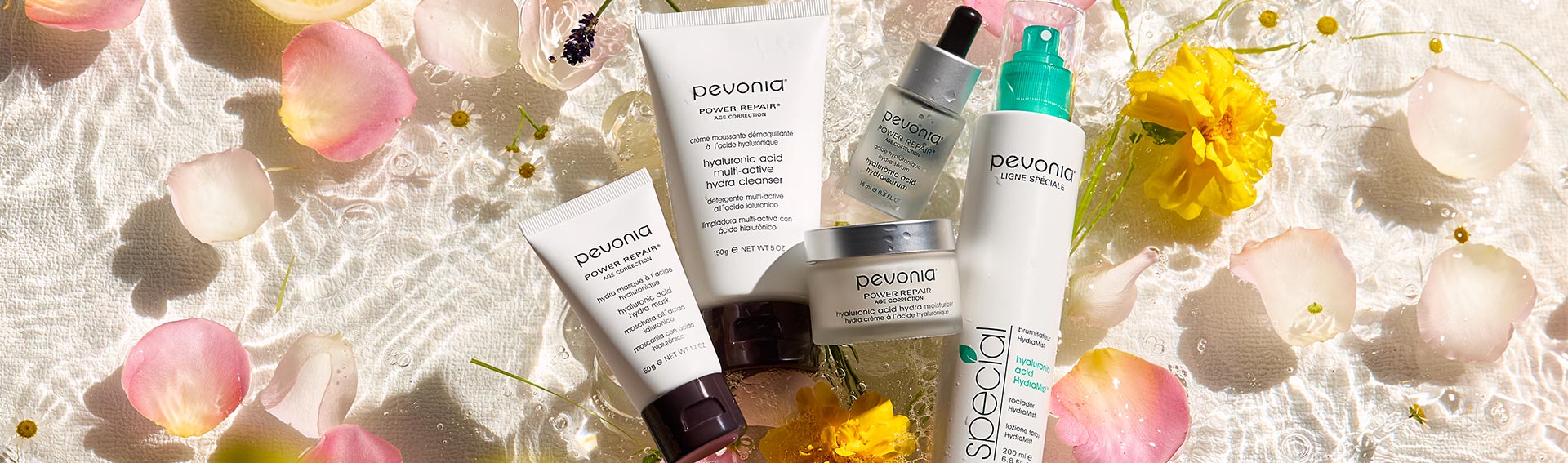 Pevonia Hyaluronic Acid Products lying in shallow water surrounded by rose petals and other floral aspects.