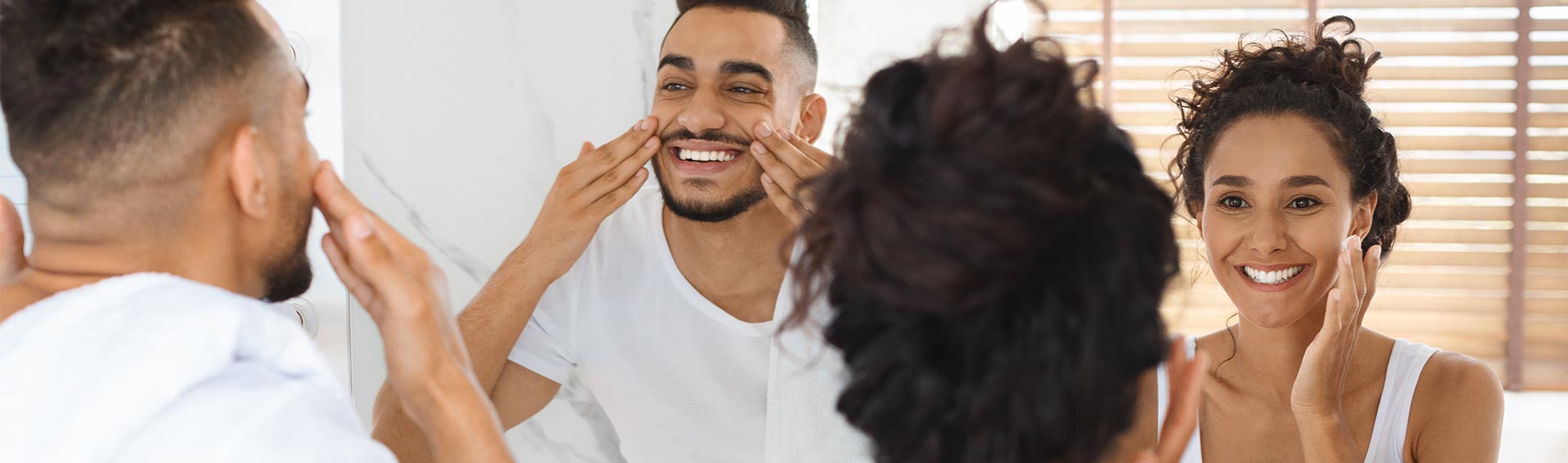 A couple performing their skincare routine in the mirror.