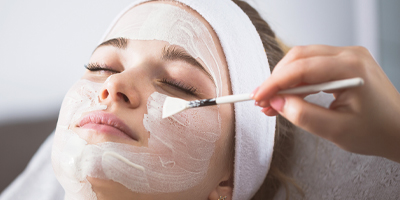 Woman receiving a facial treatment, being applied with a brush, at a spa.